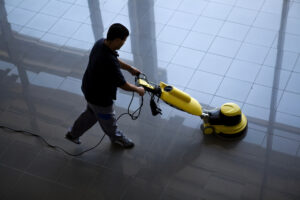 man pushing a floor care machine across shiny floor at night