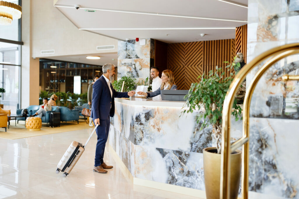 man in resort hotel lobby at reception desk greeted by hotel staff